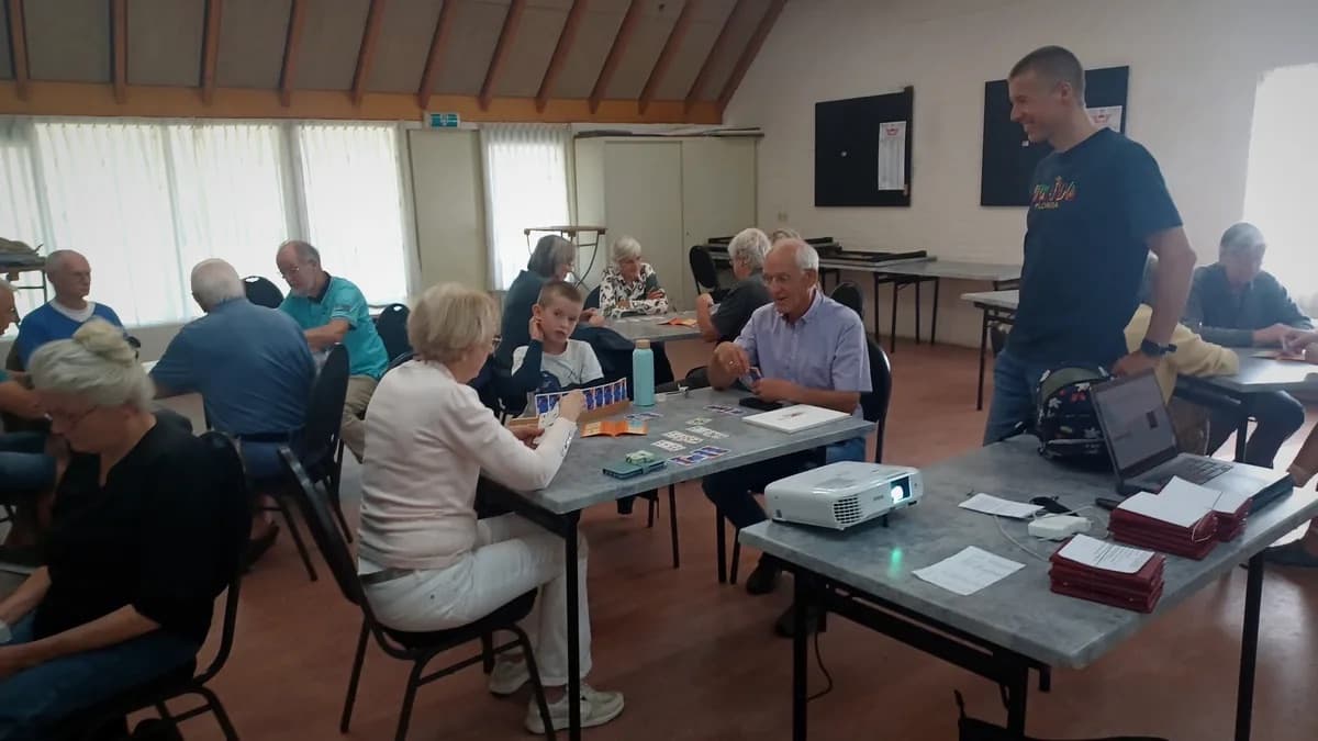 Richard Ritmeijer geeft bridgeles in een clubzaal, met spelers aan tafels met kaarten